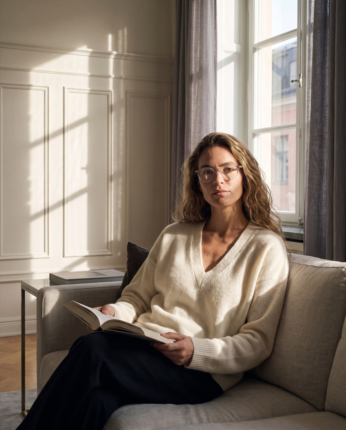 Kvinna som läser i soffan i lågt septemberljus, med läsglasögonen Emily Quartz.